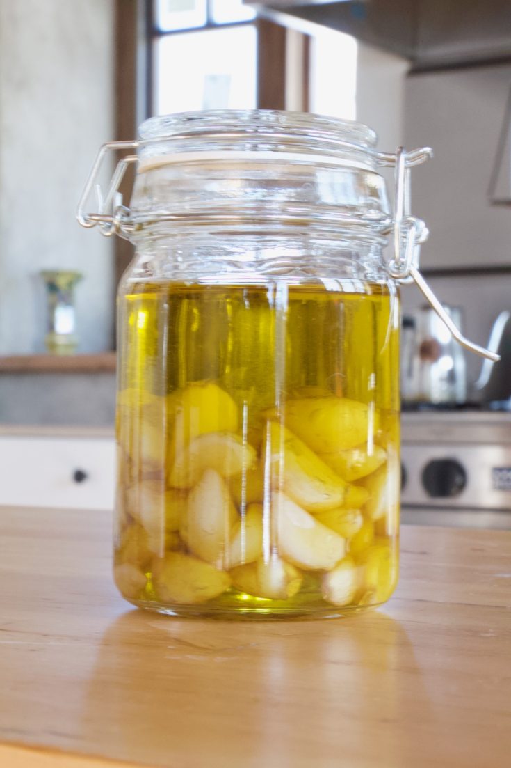 Glass flip top jar full of roasted garlic covered in olive oil