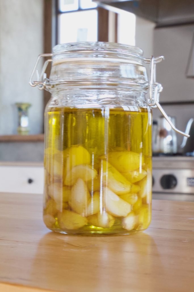 Glass flip top jar filled with roasted garlic covered in olive oil