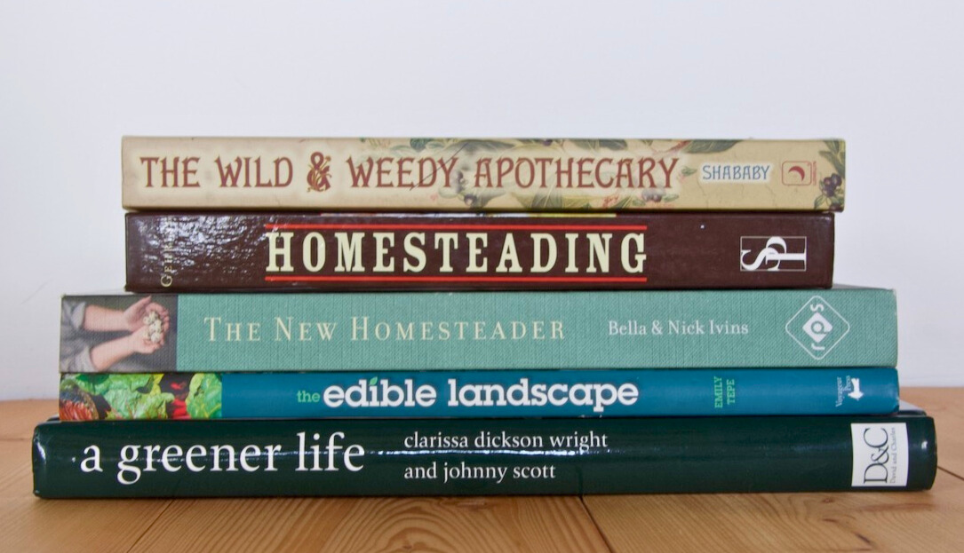 stack of homesteading books on a wooden floor with a white background