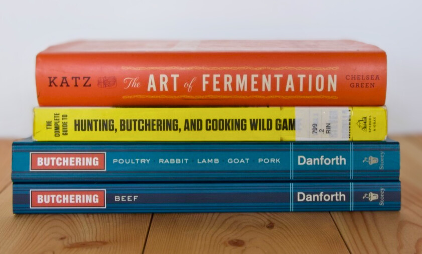 Stack of homesteading books on a wooden floor with a white background