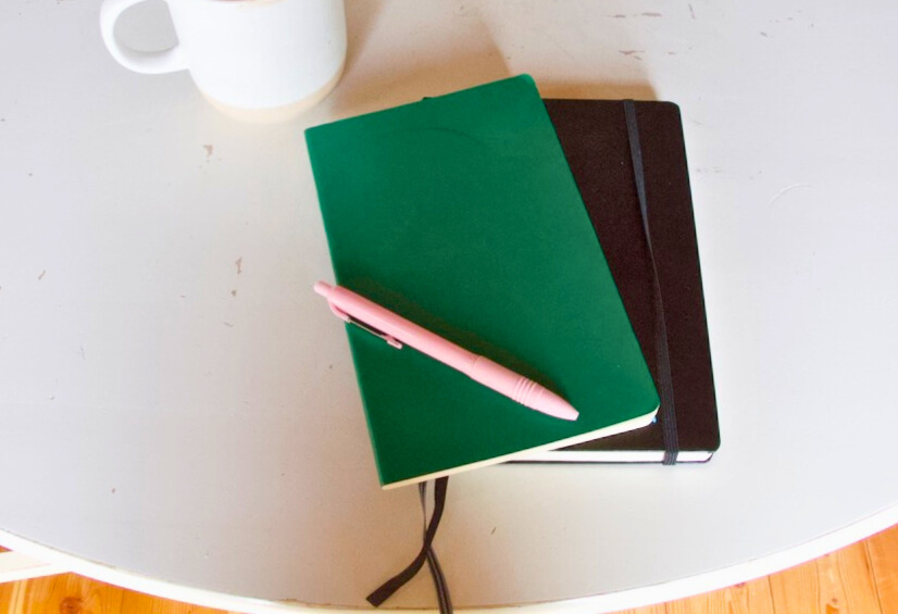 notebooks, pink pen and coffee cup on a white table top