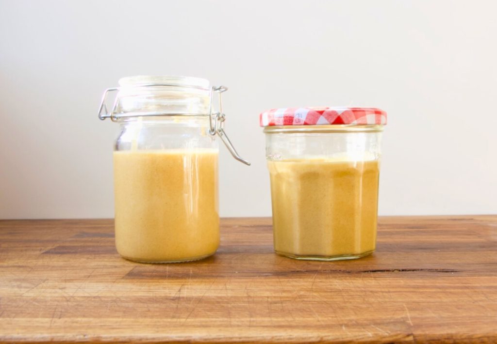 two jars of homemade hot honey mustard on a wooden board