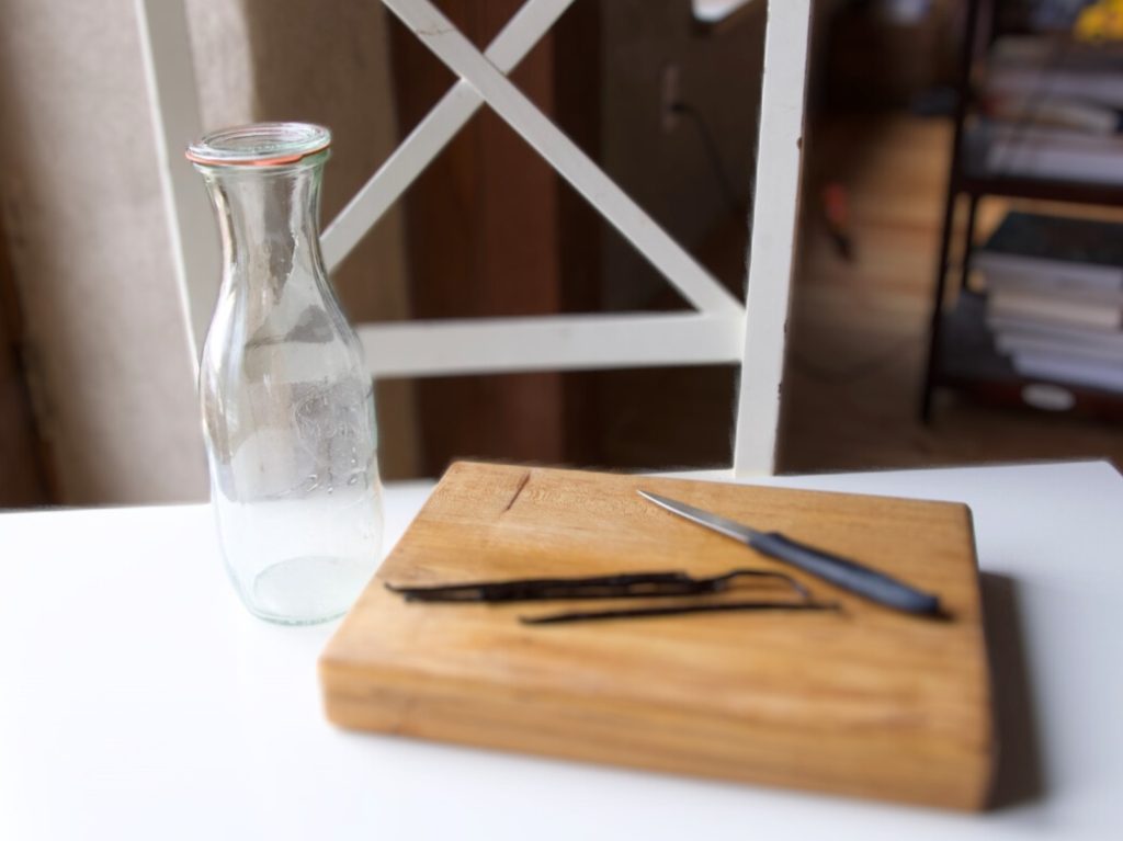 vanilla beans on a wooden cutting board with a knife and an empty glass bottle