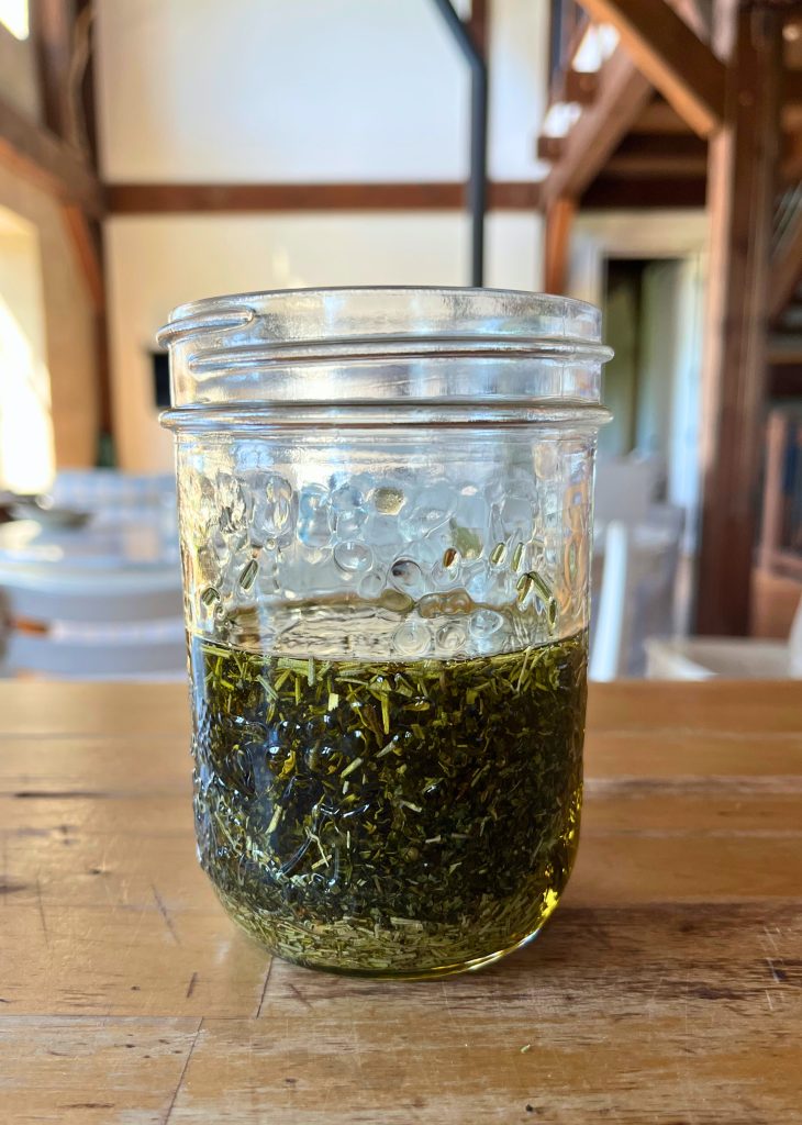 glass jared filled with dried rosemary, dried mint and olive oil on a wooden counter