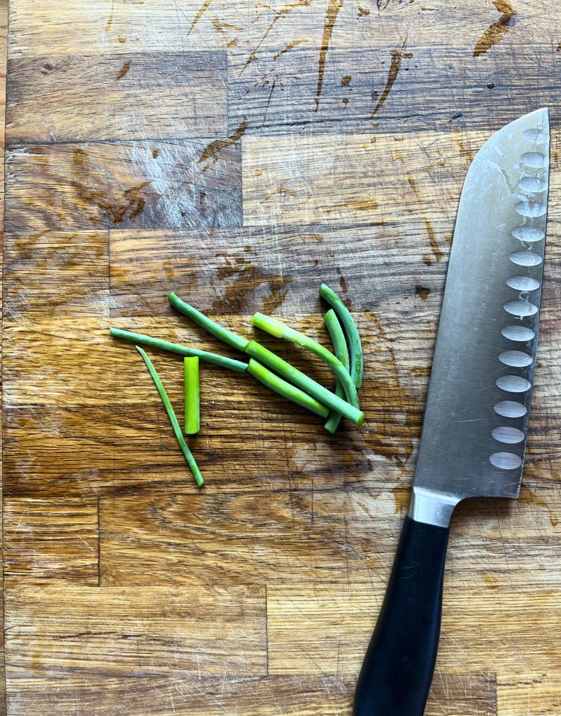 chopped garlic scapes on a wooden cutting board with a knife