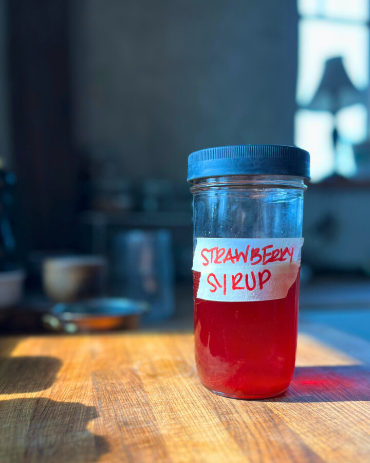 jar of strawberry syrup on a wooden cutting board