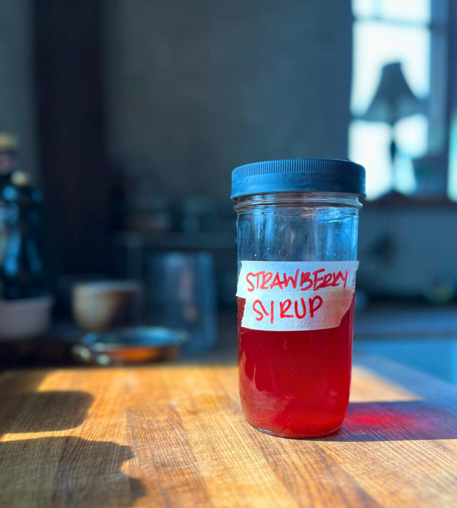 jar of strawberry syrup on a wooden cutting board